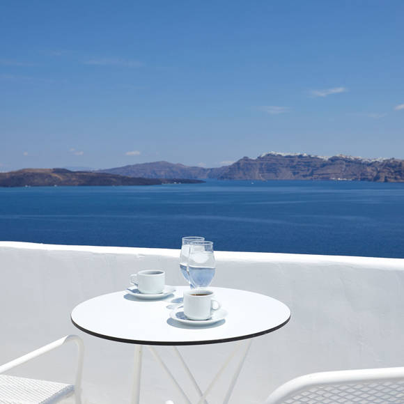 Santorini View Hotel white table seats, greek coffee and glasses of water, at a balcony with caldera sea view